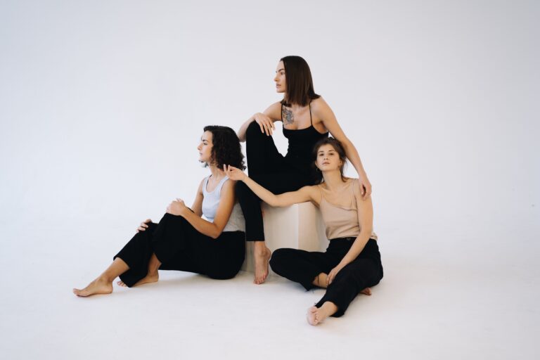 Three women sitting gracefully on the floor of a minimalist white space, showcasing elegance and modern style.